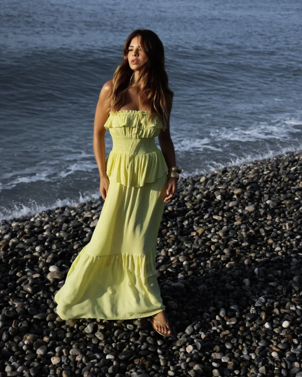 “vestido dora kaele longo com babados e lastex” “vestido longo romântico amarelo claro à beira-mar” “detalhe de babados e saia em camadas com caimento fluido”